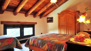 Une chambre avec deux lits, des poutres en bois, une grande armoire et une fenêtre donnant sur un beau paysage.