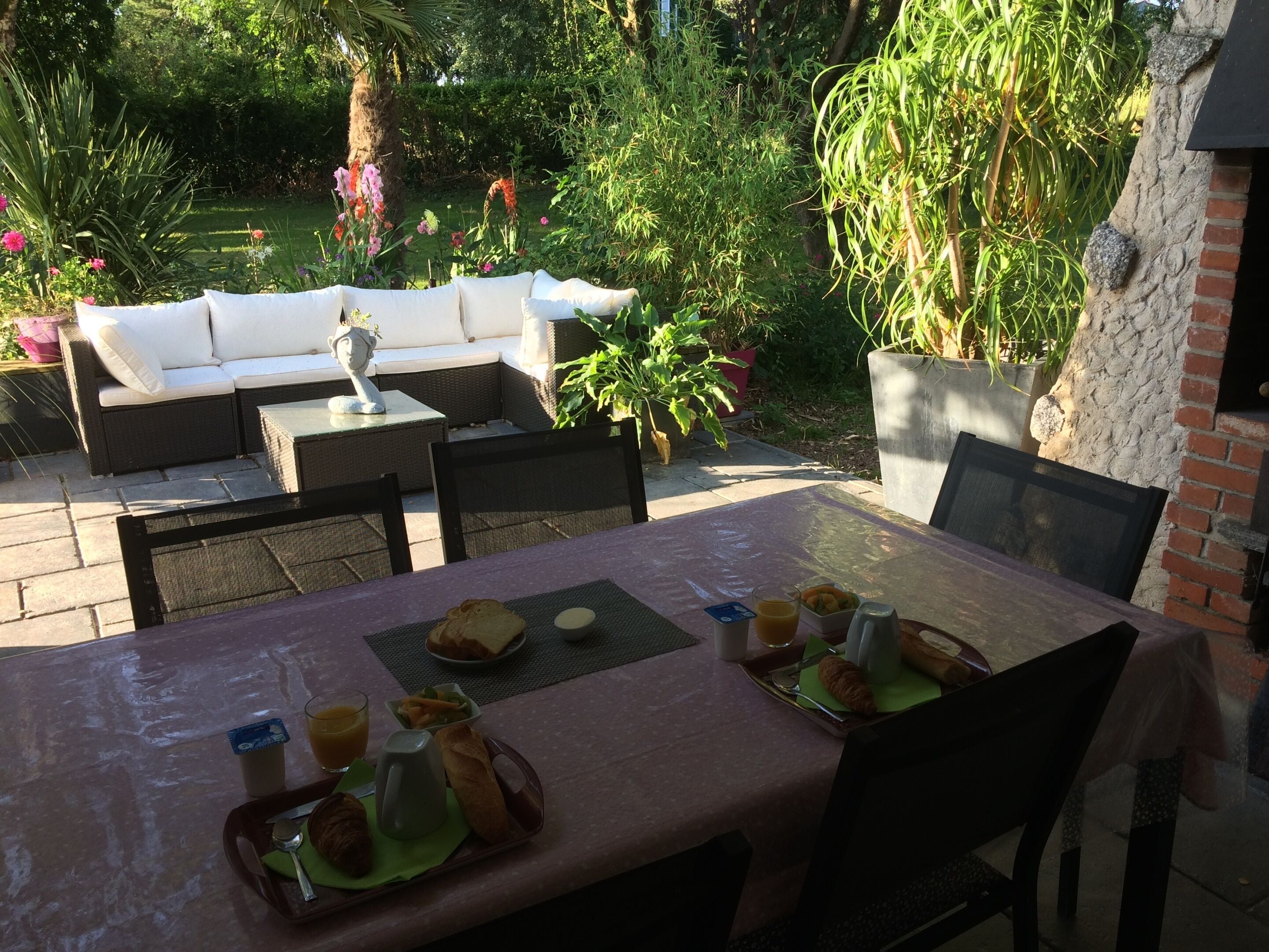 An outdoor dining area with a table set for two, surrounded by wicker furniture and potted plants.