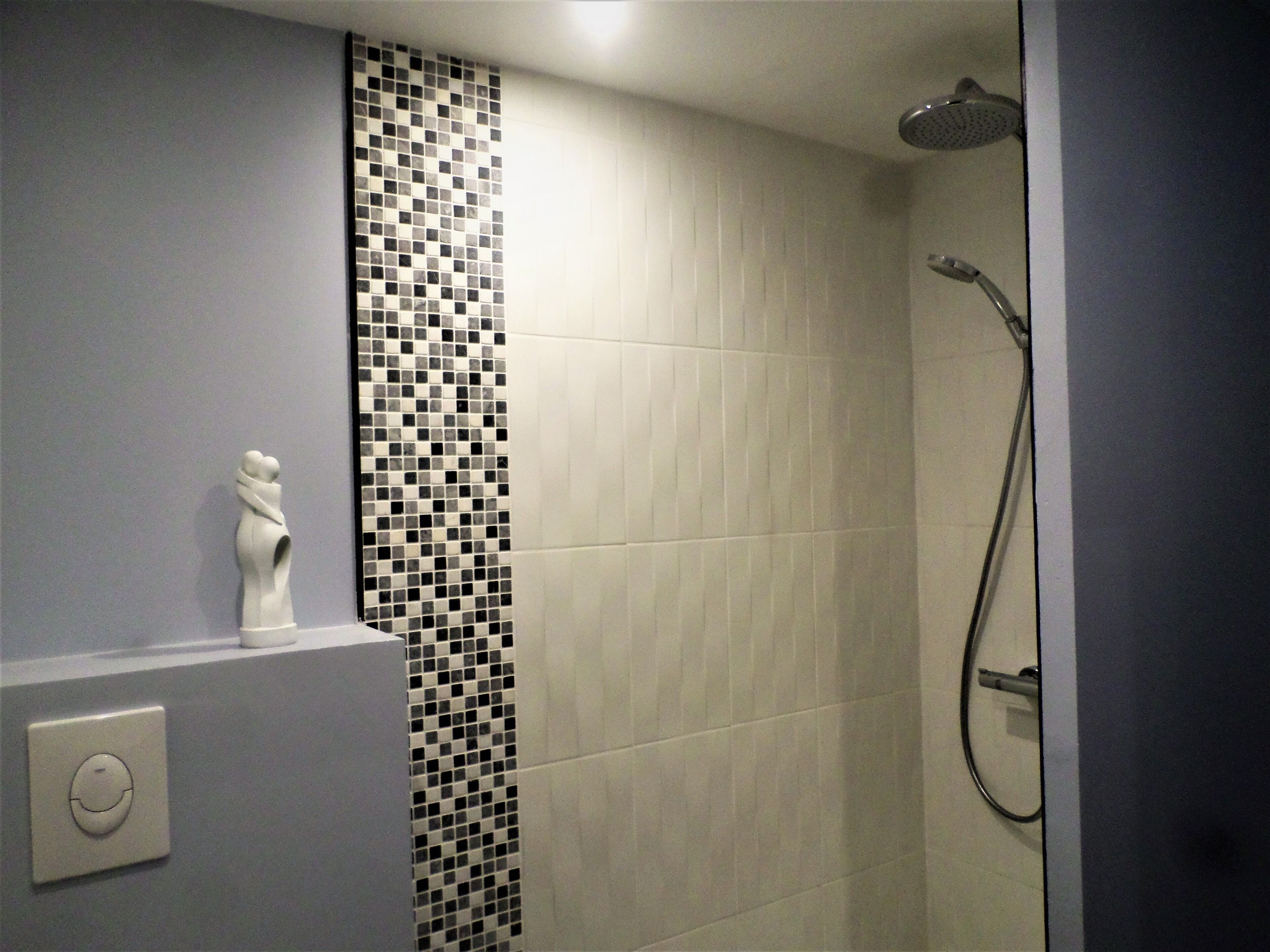A bathroom with a shower, a wall-mounted light switch, and a decorative tile pattern.