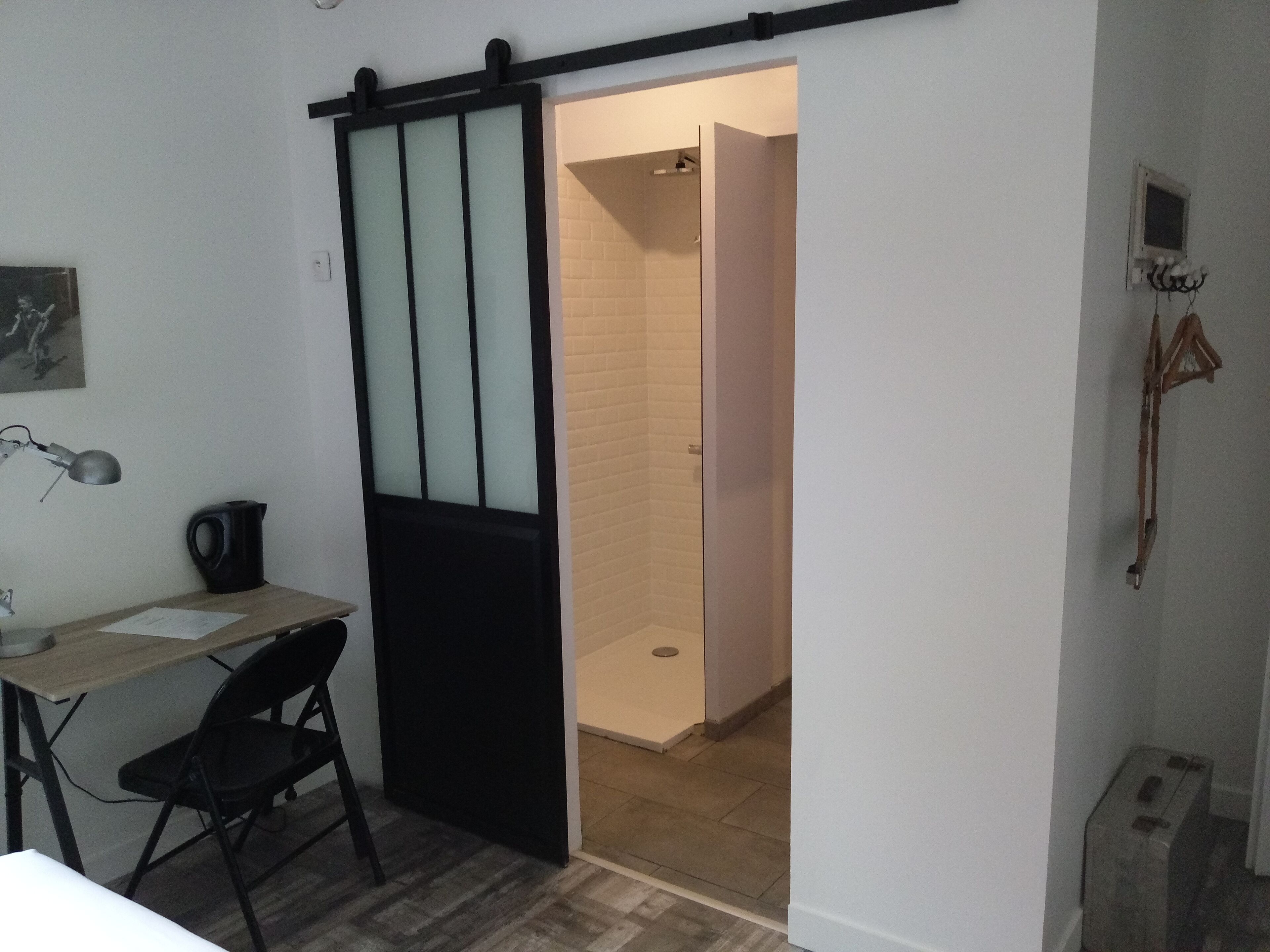 Una habitación con escritorio, silla y puerta corredera que da a una zona de ducha.