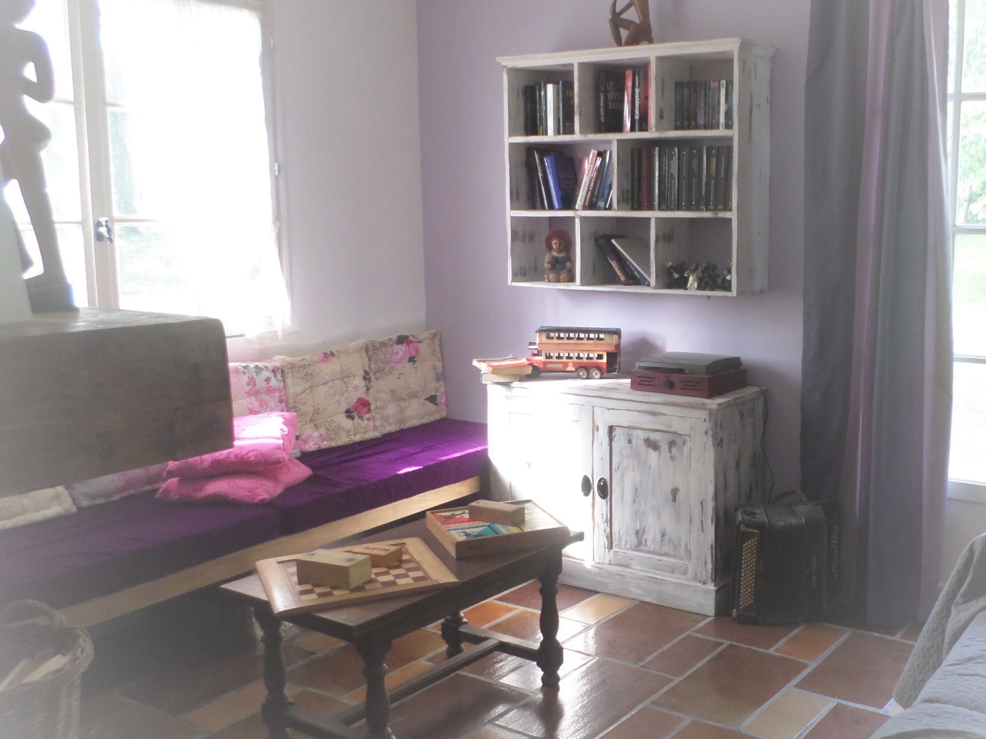 A cozy living room with a sofa, a coffee table with a chess set, a bookshelf, and a radiator.