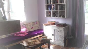 A cozy living room with a sofa, a coffee table with a chess set, a bookshelf, and a radiator.