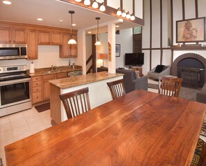 A modern kitchen with granite countertops, wooden cabinets, a large island with bar stools, a built-in oven, and a flat-screen TV.