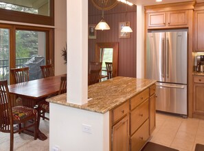 A kitchen with a granite countertop, wooden cabinets, a stainless steel refrigerator, and a dining area with a wooden table and chairs.