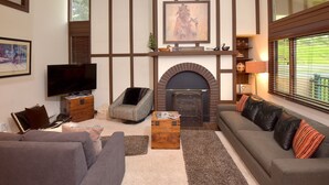 A living room with a fireplace, a sofa, a recliner, a TV, and a bookshelf. - Vantage Point 210 3 Bedroom Condo by RedAwning (Vail)