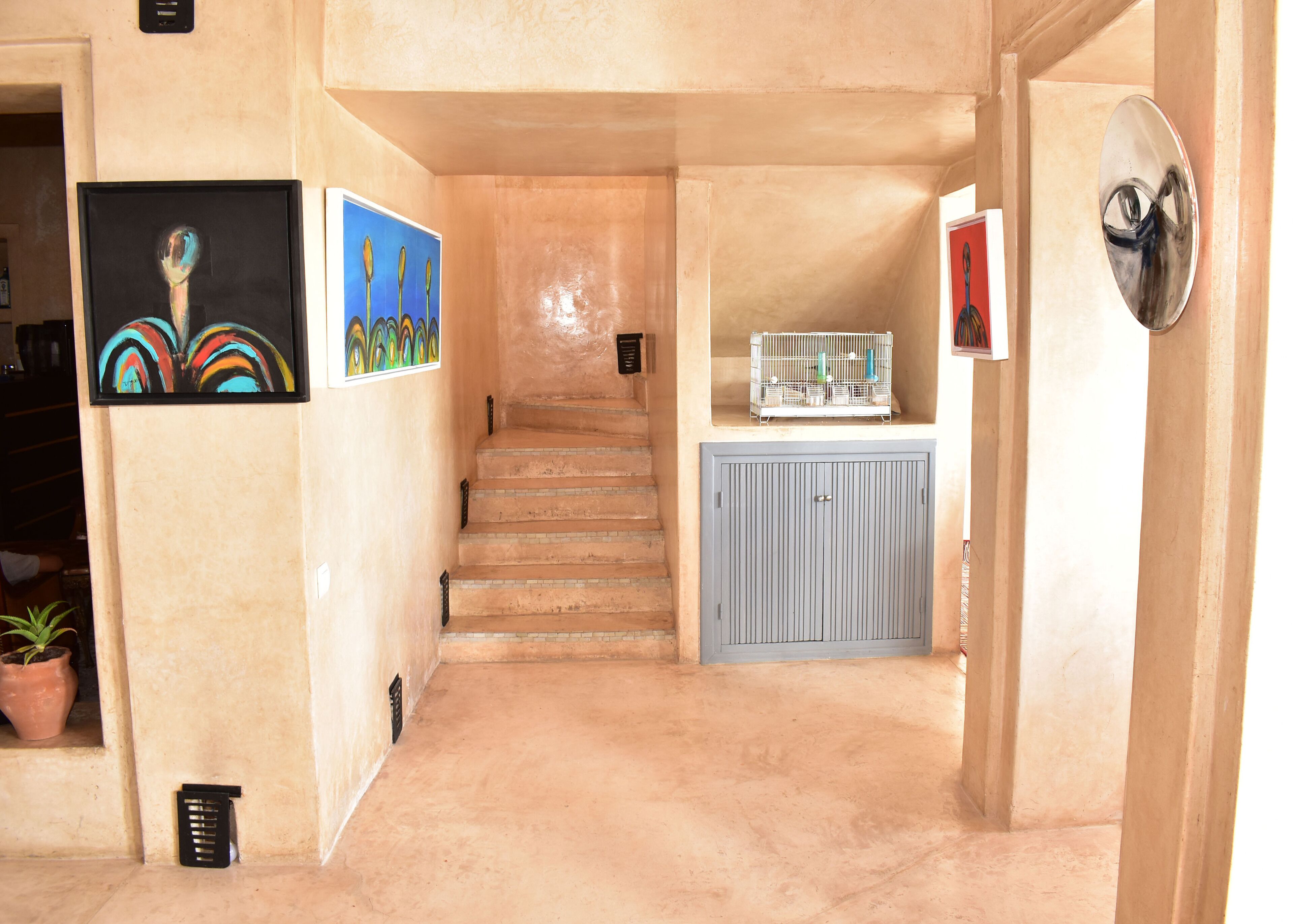 Een gang met een trap, kunstwerken aan de muur, een blauwe kast en een potplant.
