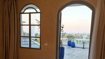 Habitación de hotel con un gran ventanal de arco, una cama y vistas al área exterior con plantas en macetas.