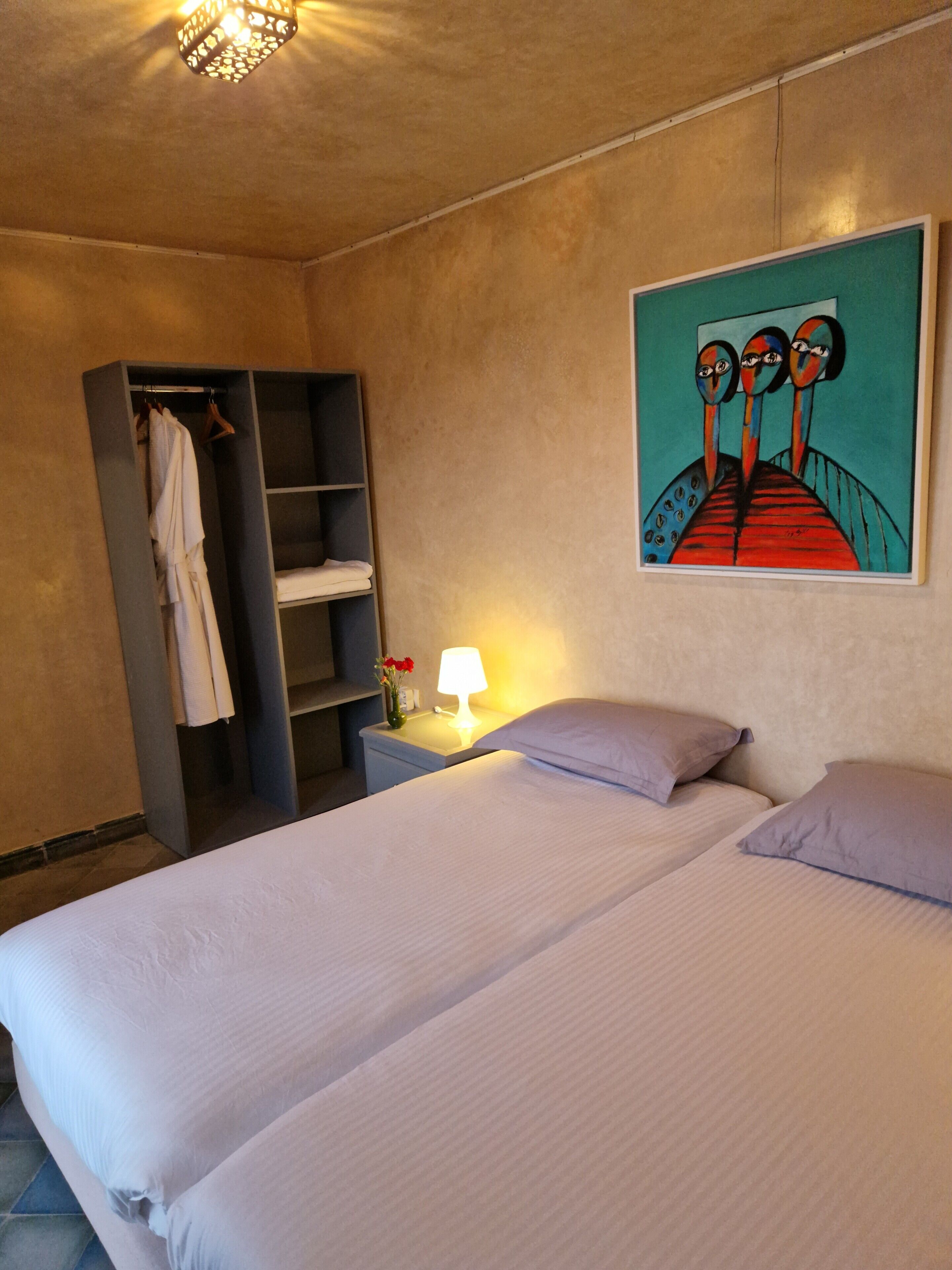 Una habitación de hotel con cama, mesita de noche con lámpara, armario y un cuadro en la pared.