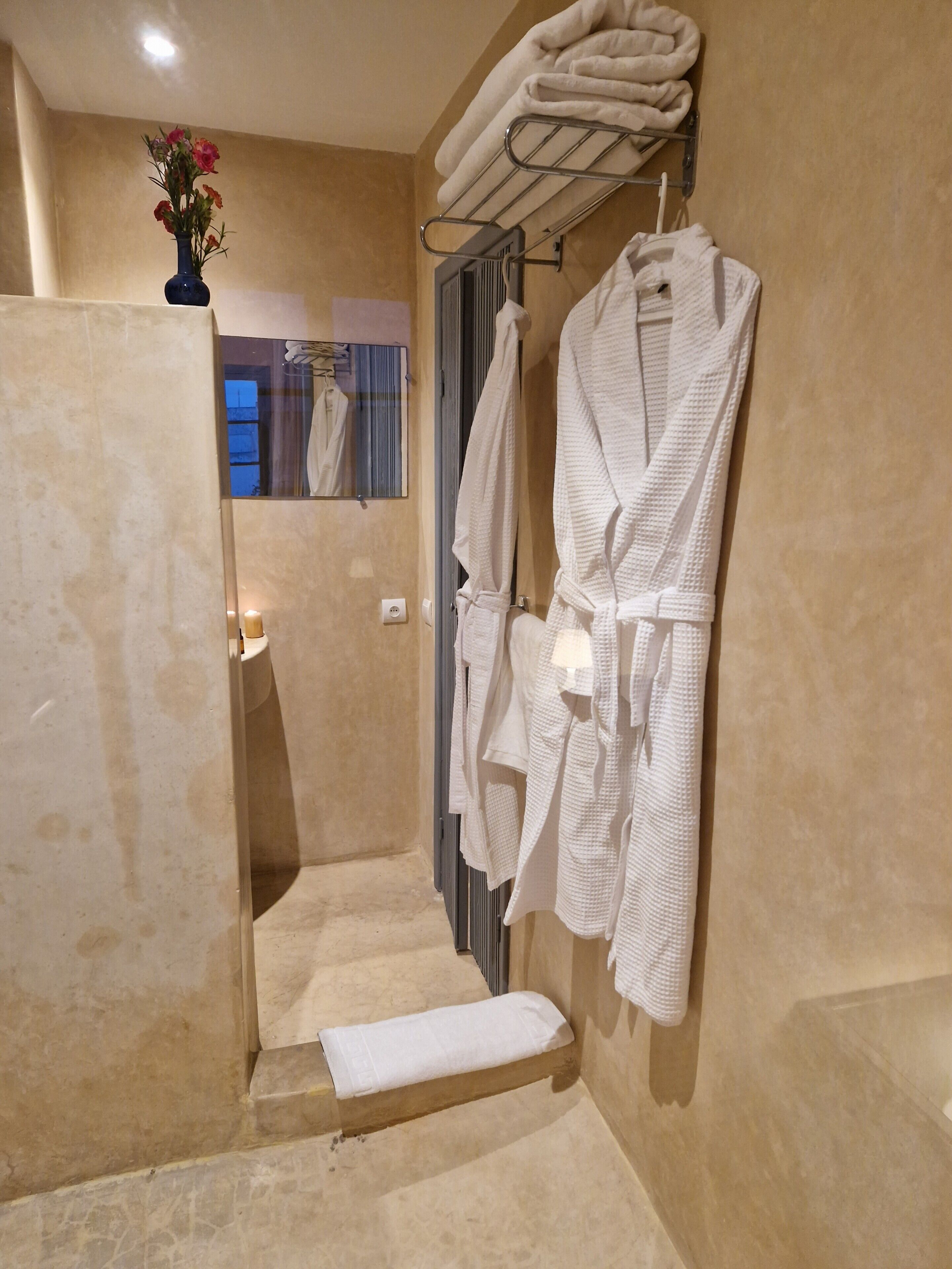 Un baño con bañera, un perchero con batas y un florero con flores.