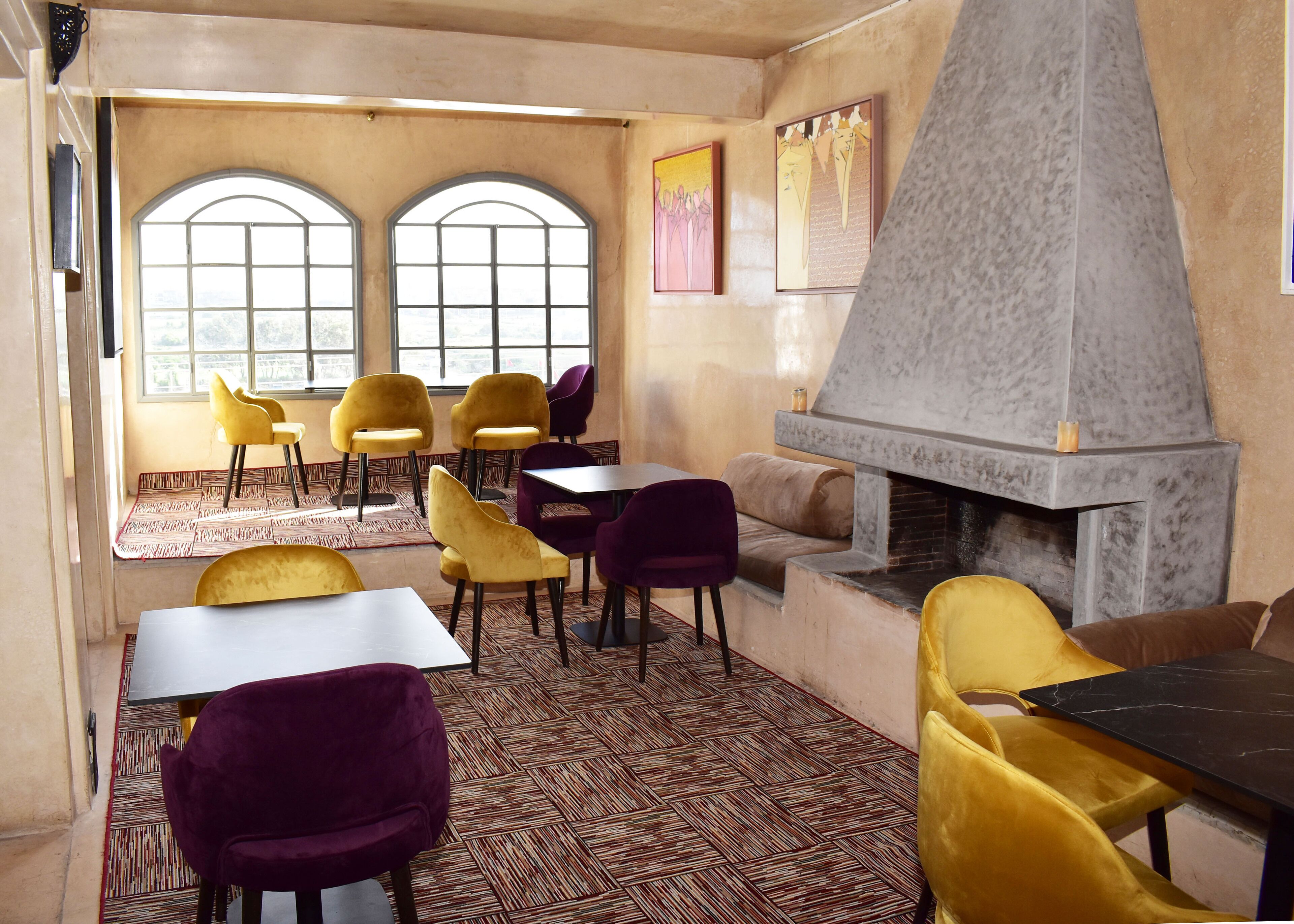 A restaurant with a fireplace, yellow and purple chairs, and large windows.