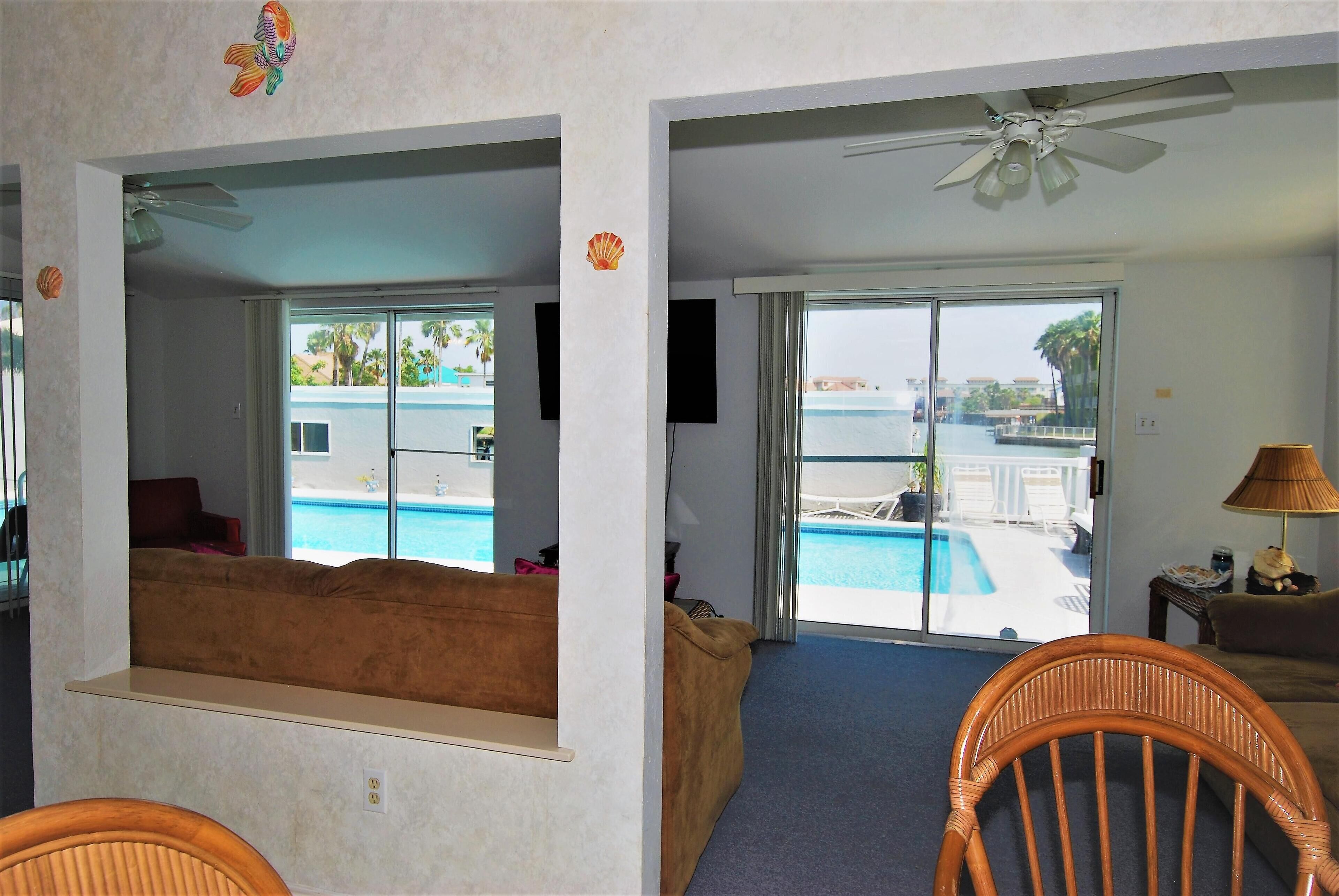 A room with a view of a pool, a ceiling fan, and a sofa.