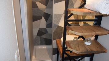 Une salle de bain avec un mur de douche orné d’un motif géométrique, une étagère en bois sur laquelle est posée une serviette roulée, et un petit bocal en verre.