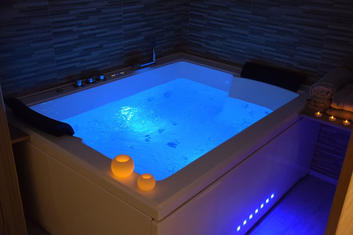 A modern spa tub with a built-in heater, two candles, and a wooden bench.