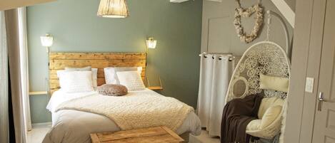 Une chambre à coucher avec une tête de lit en bois, un grand lit avec une literie blanche, une commode en bois et un fauteuil décoratif.