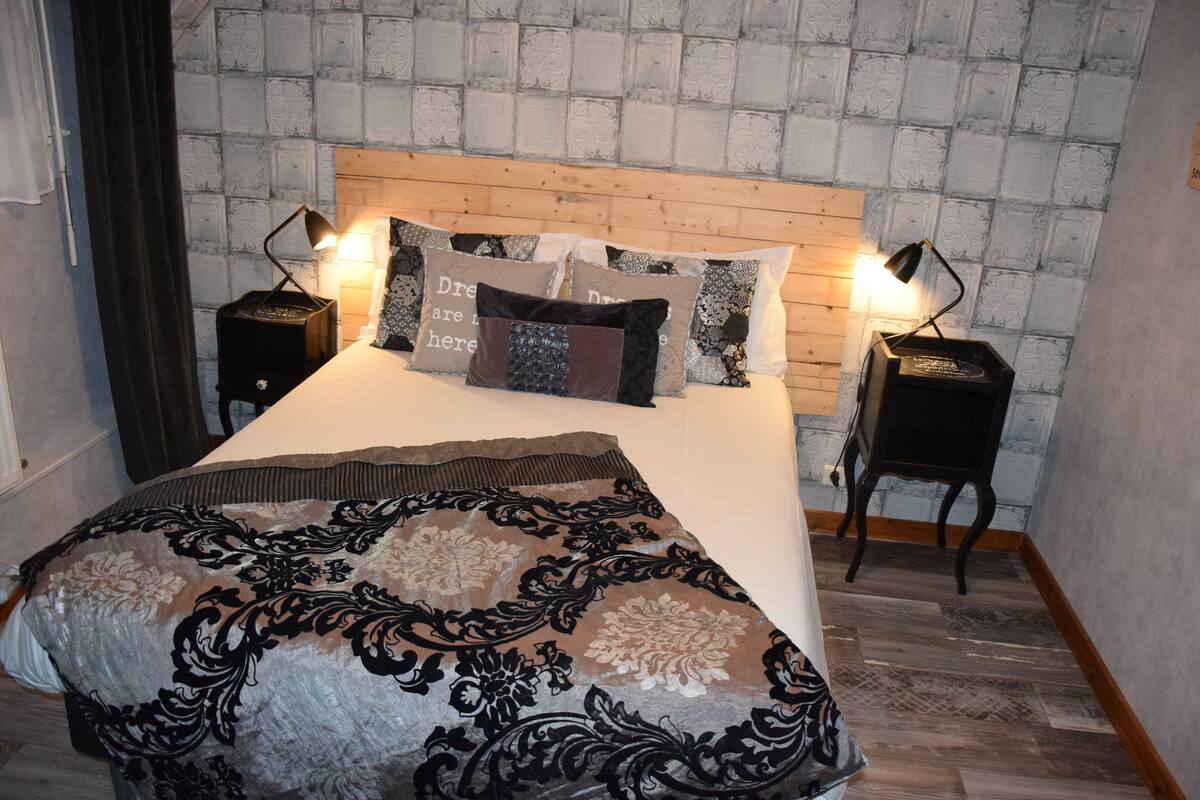 A neatly made bed with a patterned bedspread, two bedside tables with lamps, and a brick-patterned wall behind the bed.