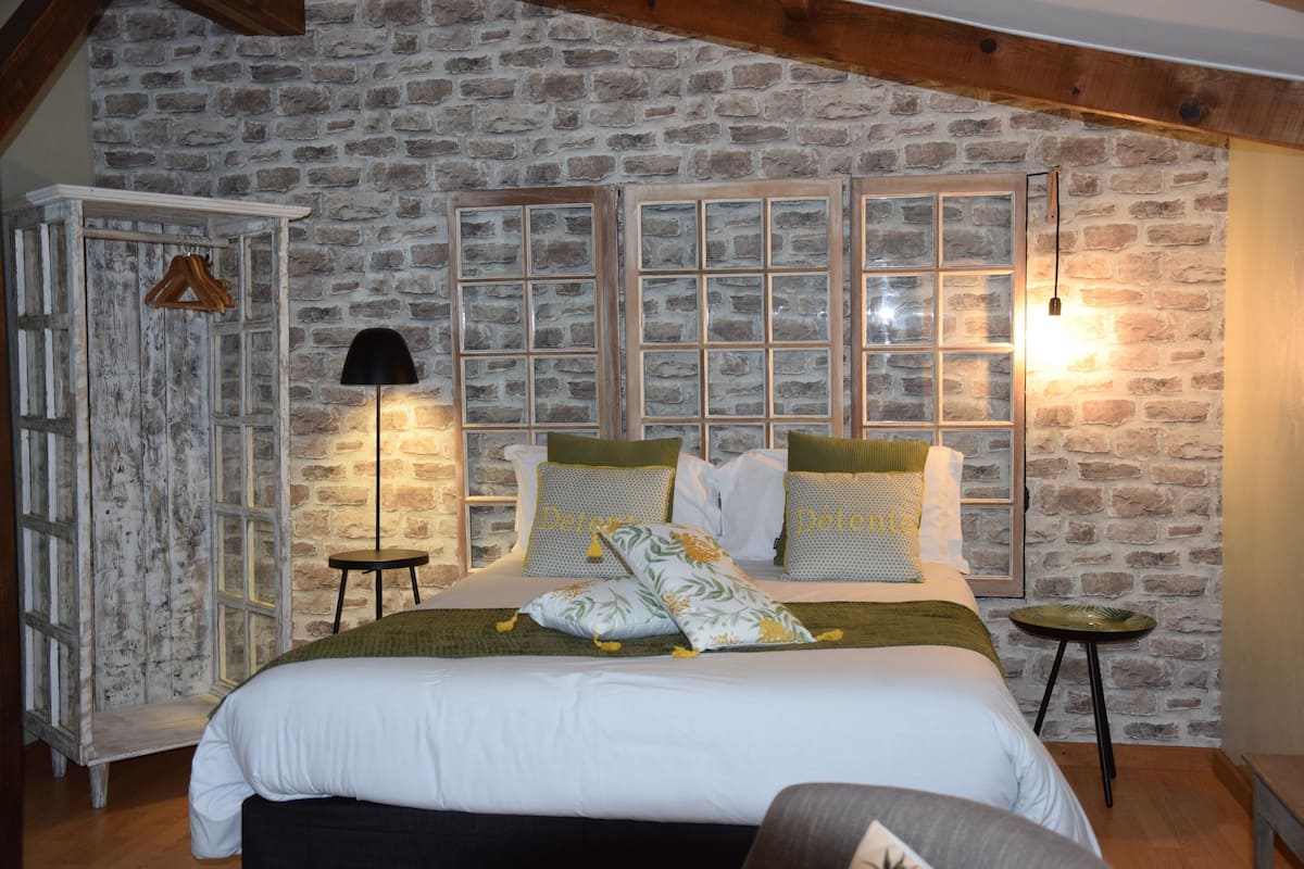 A bedroom with a stone wall, a bed with white bedding, two bedside tables, and a hanging coat rack.