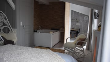 A bedroom with a large bed, a white rocking chair, a bathtub, and a small table with a chair.
