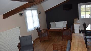 A cozy room with a wooden ceiling, a sofa, two wooden chairs, a table, and a window with curtains.