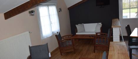 Een gezellige kamer met een houten plafond, een bank, twee houten stoelen, een tafel en een raam met gordijnen.