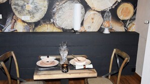 Une table à manger dressée avec des assiettes, des verres et un chandelier, le tout mis en valeur par un décor de troncs d’arbres.