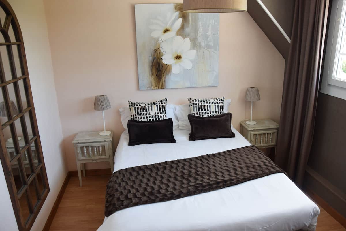 A neatly arranged bedroom with a large bed, two bedside tables, a lamp on each, and a painting above the bed.