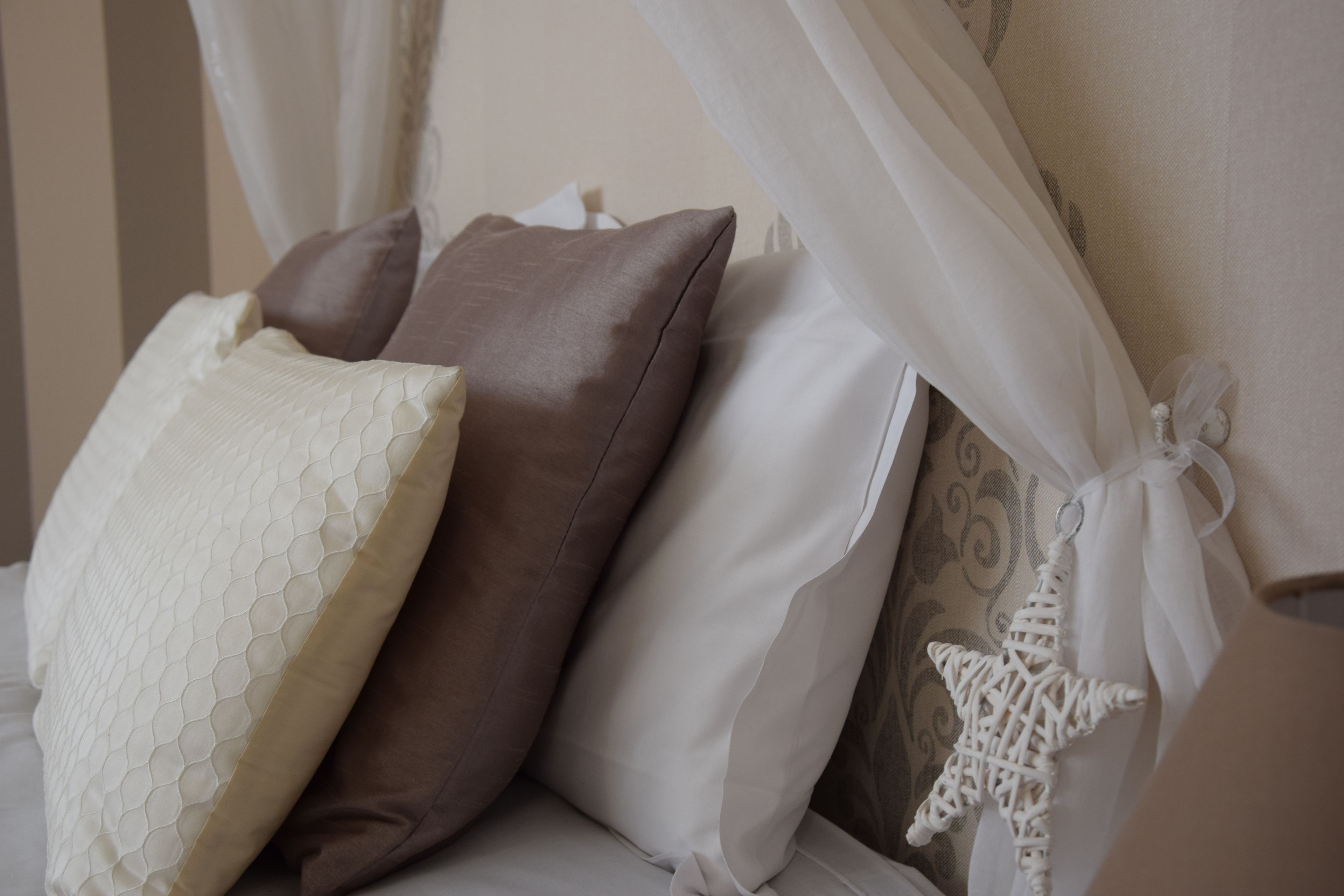 A bed with a white and brown pillow arrangement, a white star-shaped decoration, and sheer curtains.