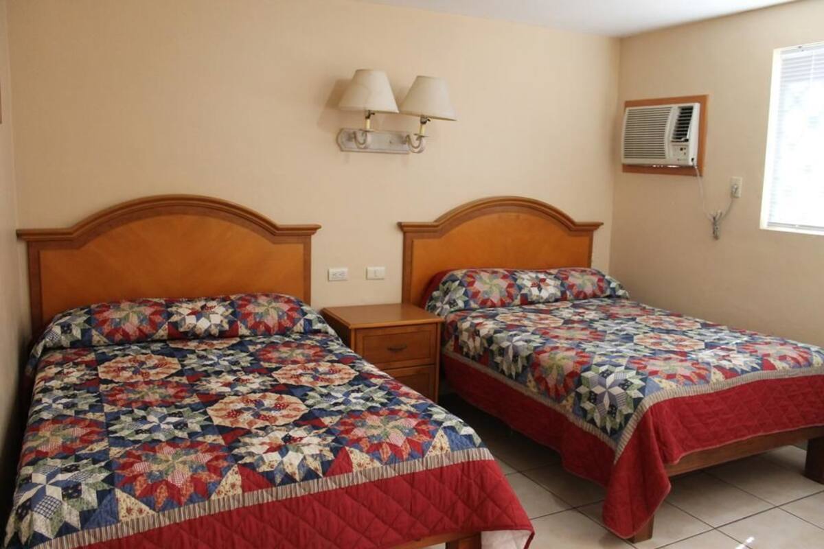 Un dormitorio con dos camas, cada una con colcha acolchada, una mesita de noche, lámparas de pared y un equipo de aire acondicionado.