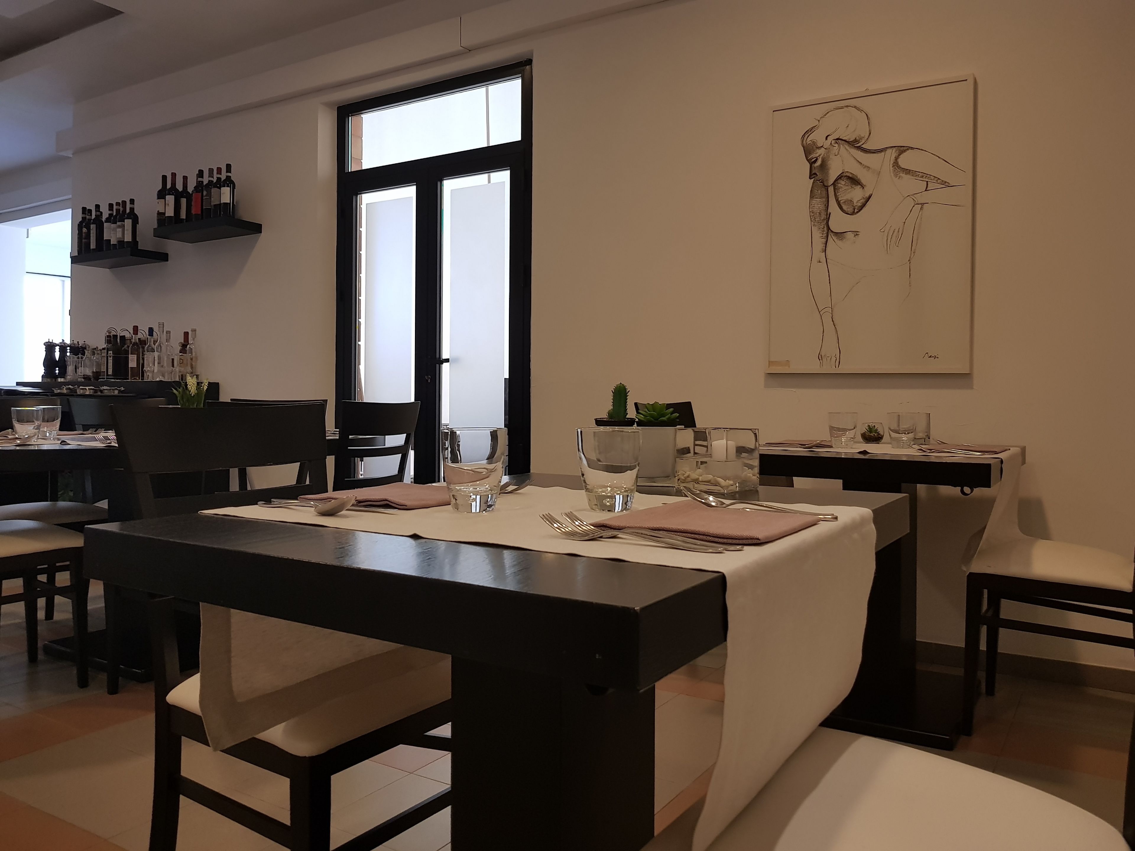 A dining area with a table set for two, a wine rack with bottles, and a large abstract painting on the wall.