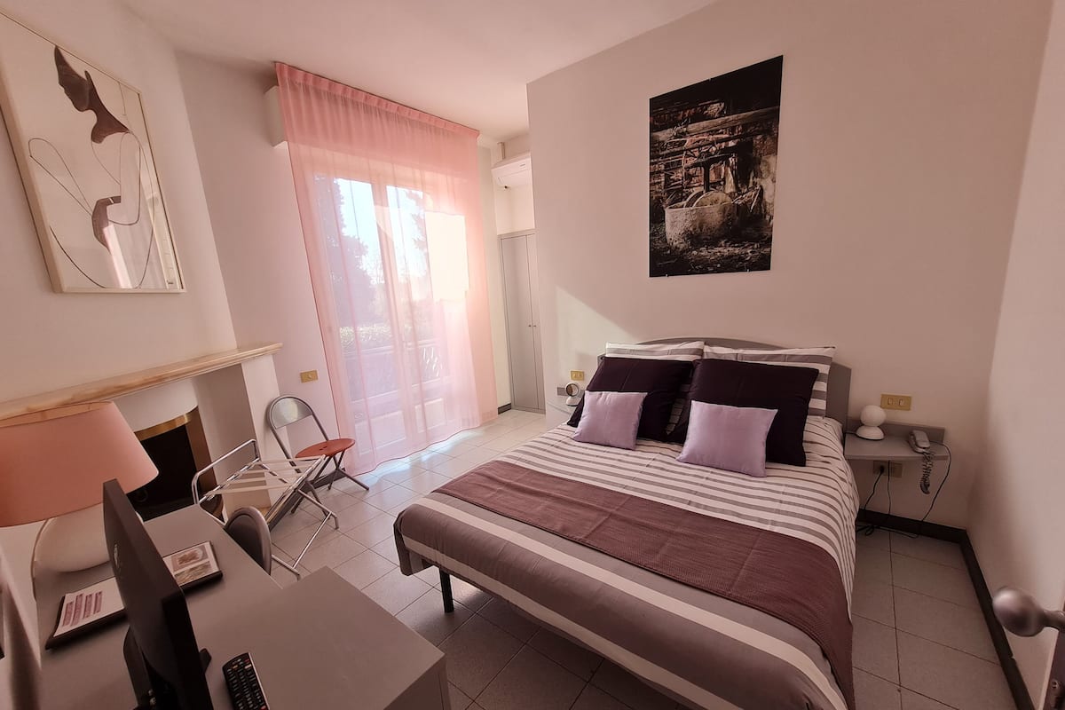 A bedroom with a bed, bedside table, chair, desk, and a window with curtains.