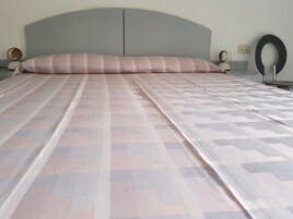 Un letto rifatto con cura, con una coperta a fantasia, una testiera sagomata, lampade sui comodini e un punto luce a parete.