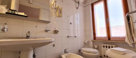 A bathroom with a sink, bidet, toilet, and a window with curtains.