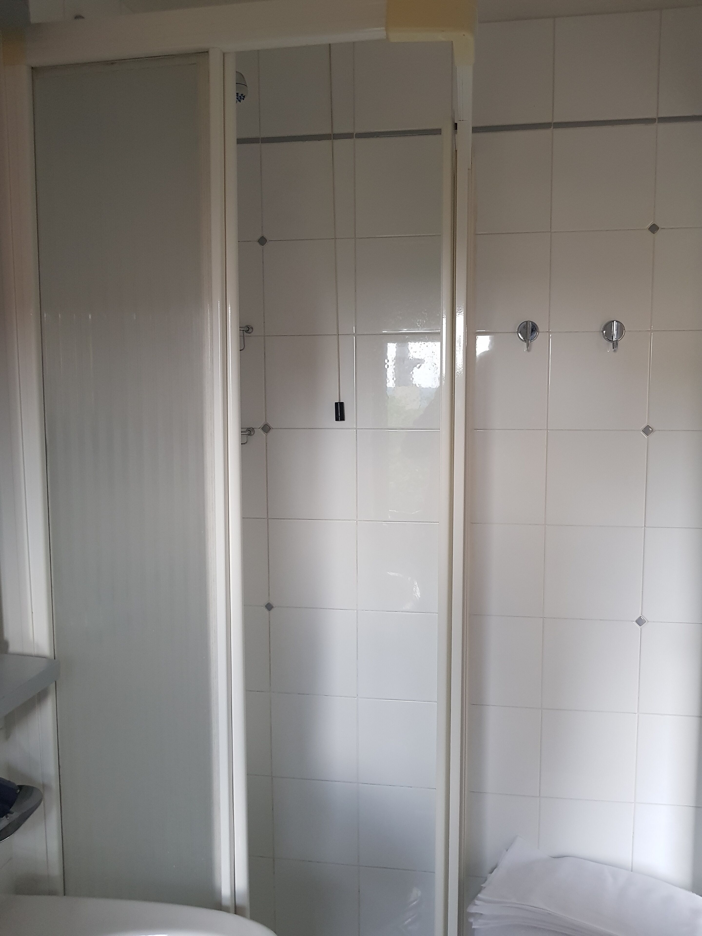 Een badkamer met witte betegelde wanden, een douchegedeelte en een toilet.