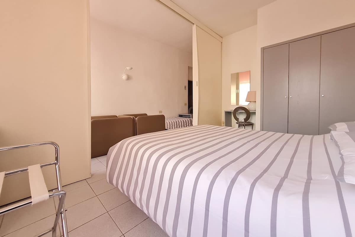 A hotel room with a bed, a desk, a chair, a wardrobe, and a lamp.
