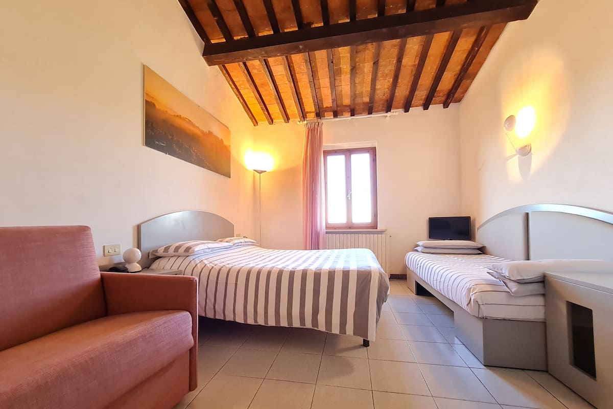 A room with two beds, a sofa, a painting on the wall, and a window with curtains.