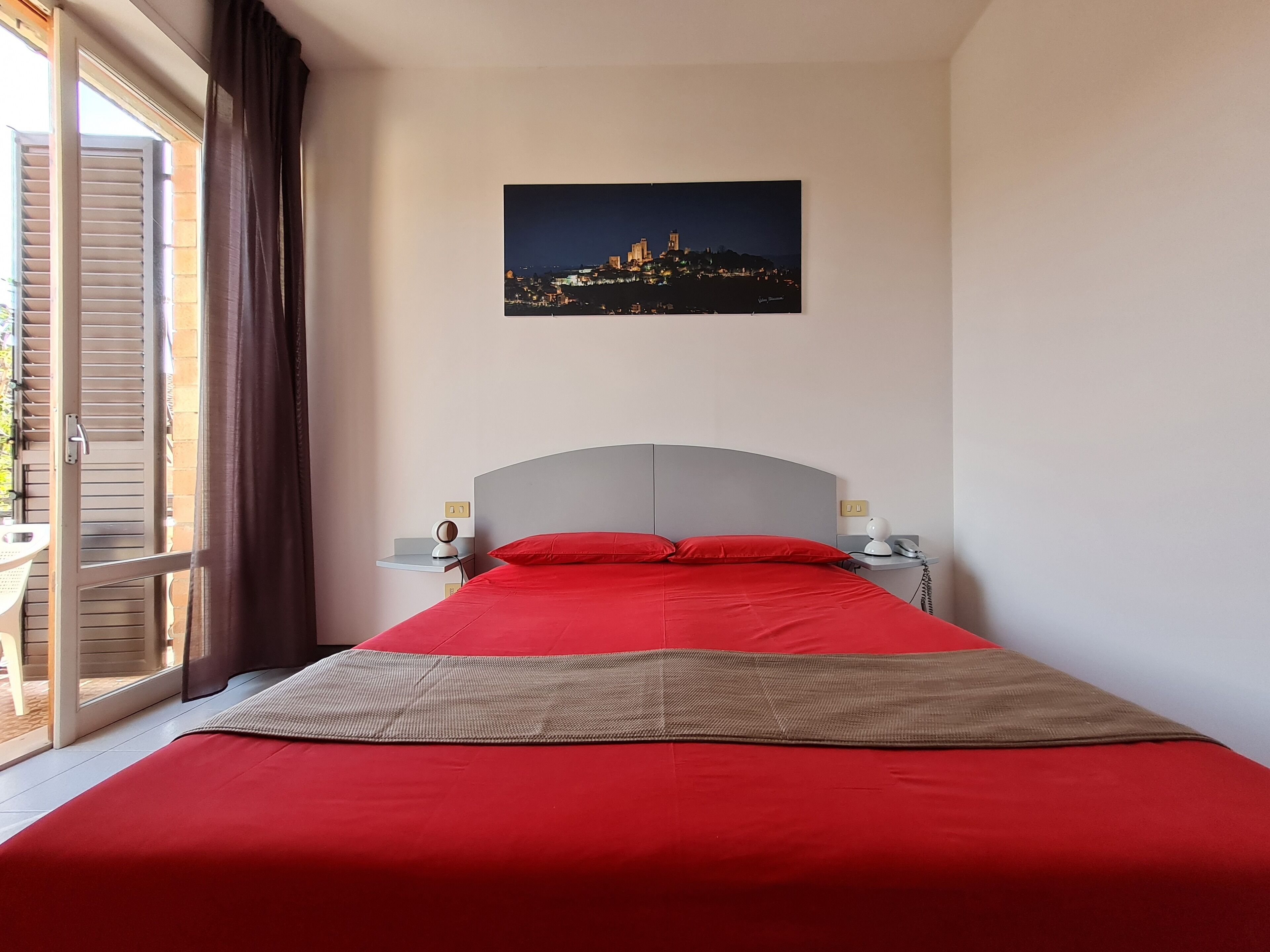 A hotel room with a bed, a nightstand, a lamp, and a cityscape view.