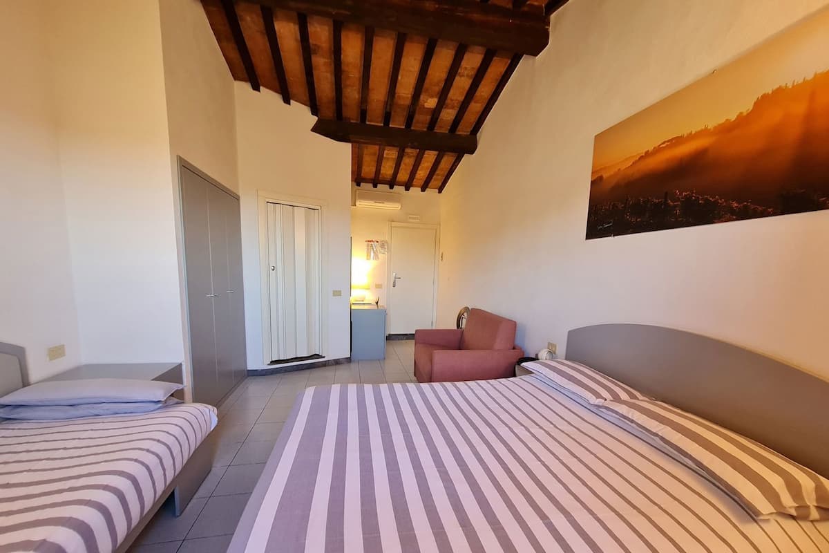 A hotel room with two beds, a wooden ceiling, a painting, and a small seating area.