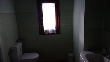 Un bagno piccolo e poco illuminato, con il water, un lavandino e una finestra con tenda.