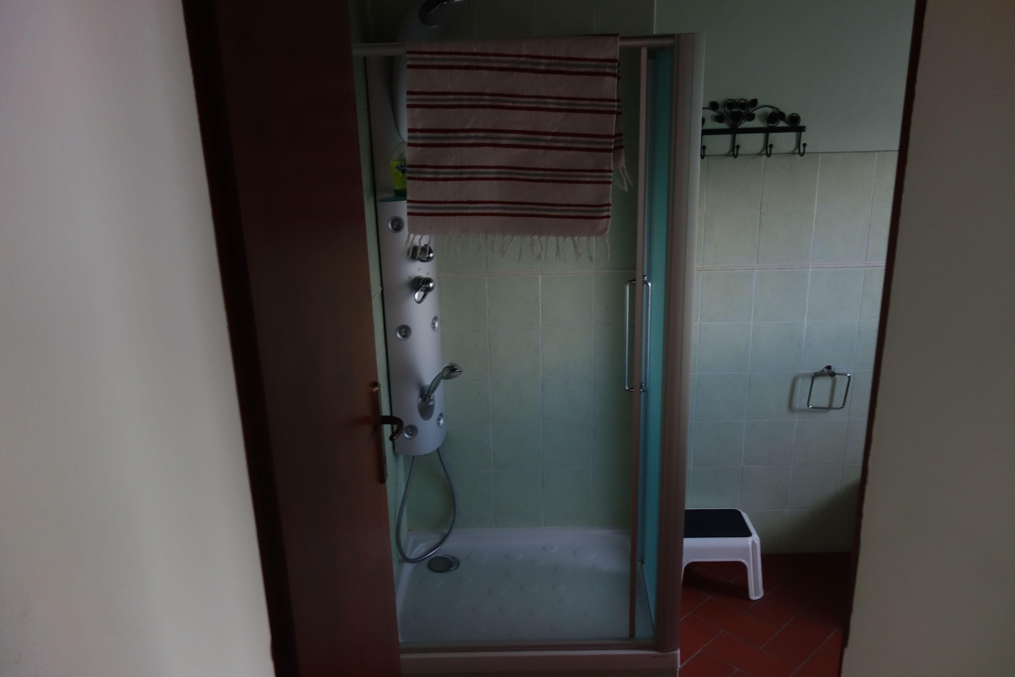 Una ducha con puerta de vidrio, una toalla colgada en la puerta y un taburete pequeño en la esquina.