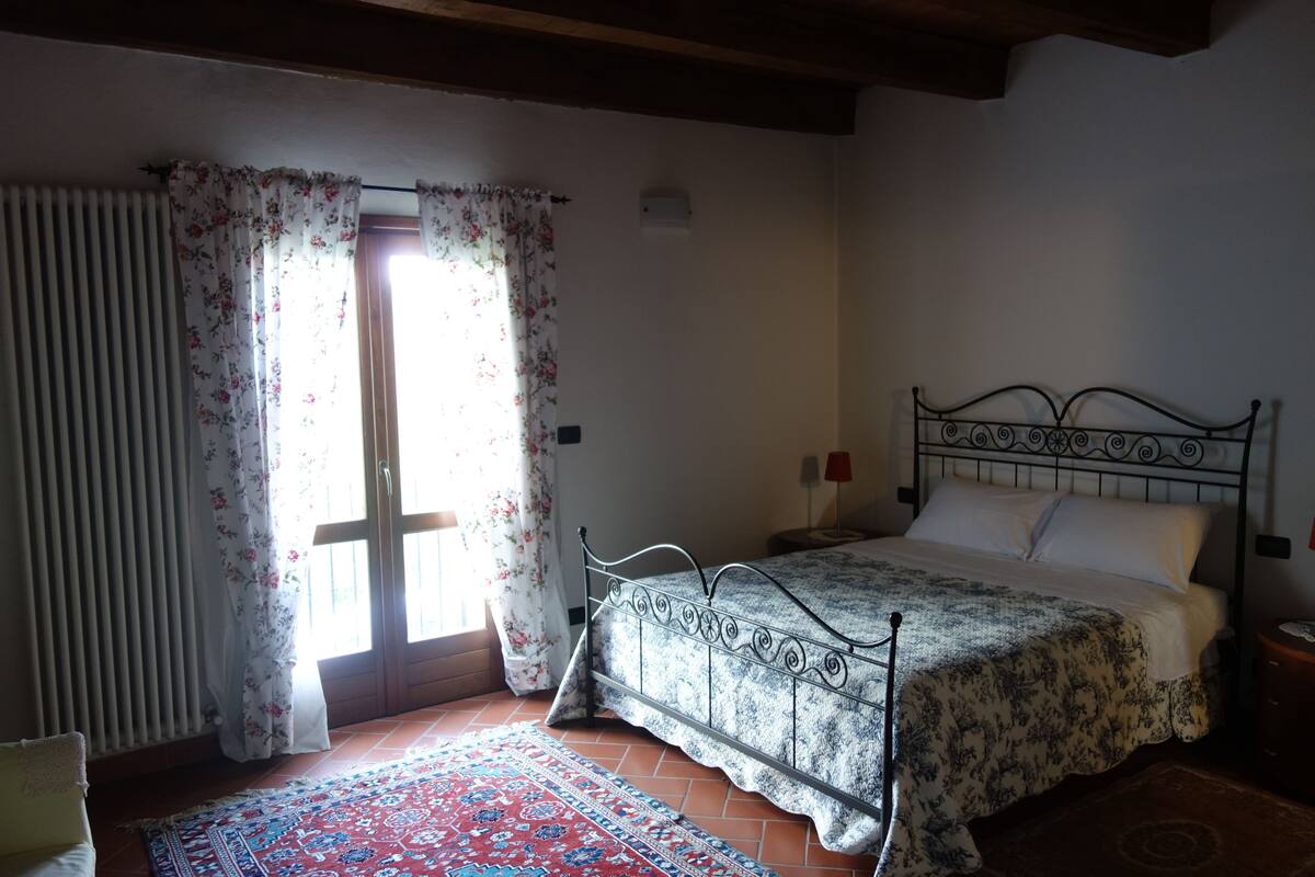 A bedroom with a bed, a window with curtains, a radiator, and a patterned rug.