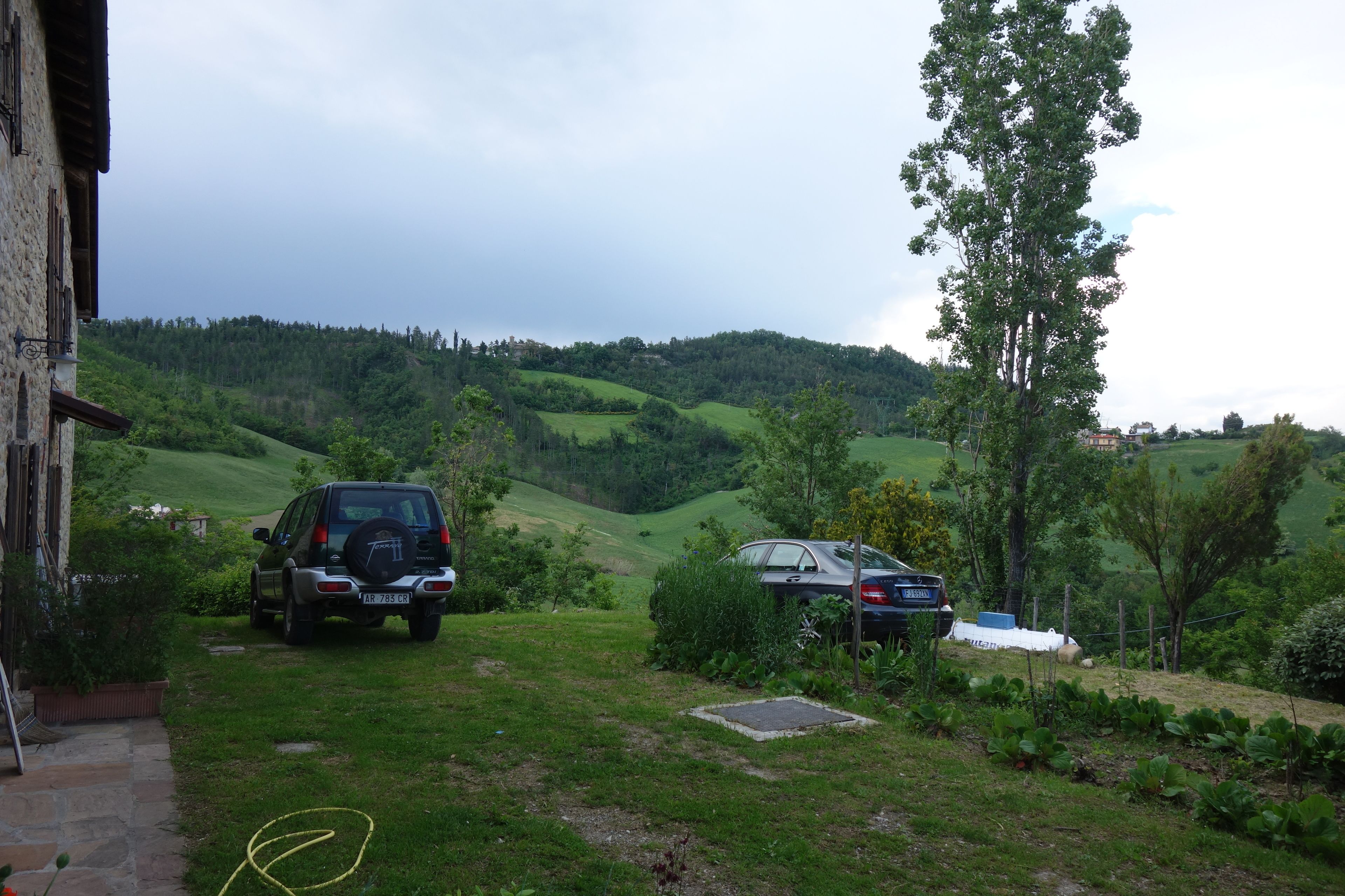 Paisaje rural con dos coches aparcados, un edificio de piedra y colinas onduladas al fondo.