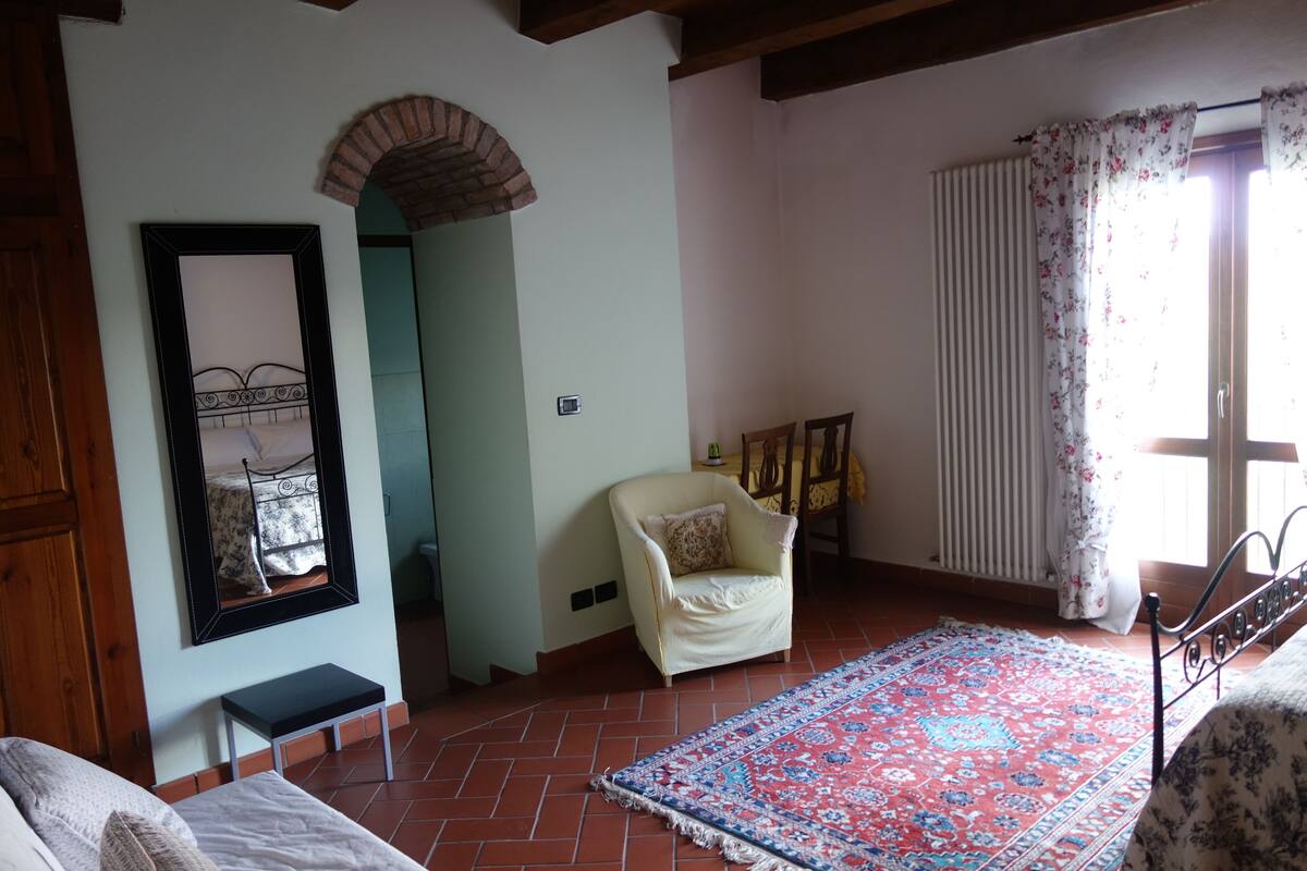 A bedroom with a bed, a chair, a rug, and a mirror.