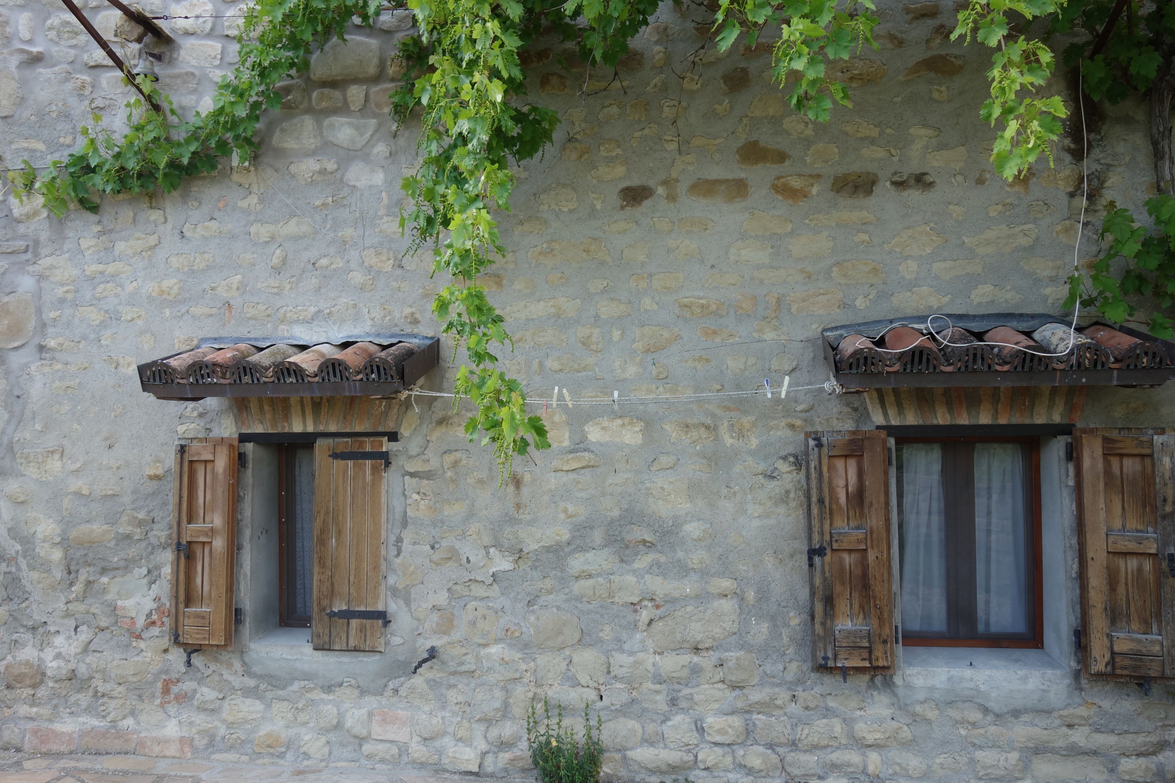 A stone building with two windows, each with wooden shutters and a tiled roof.