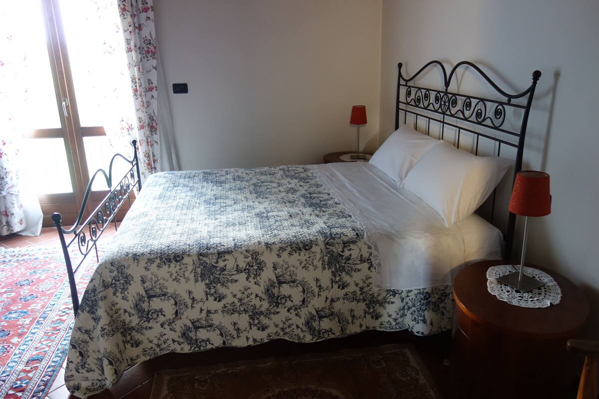 A bed with a floral bedspread, a nightstand with a red lamp, and a patterned rug.