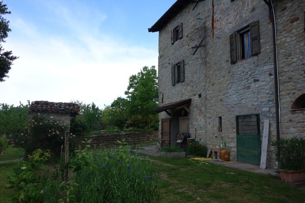A stone building with a rustic exterior, a small garden with flowers, and a wooden structure with a tiled roof. - Bed and breakfast Monte Bibele (Monterenzio)