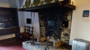 A stone fireplace with a metal mantelpiece, a wooden bench, and a small table with a television. - Bed and breakfast Monte Bibele (Monterenzio)
