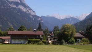 A rural setting with a large building, possibly a hotel, surrounded by lush greenery and mountains in the background. - Haus Alpenrose (Waidring)