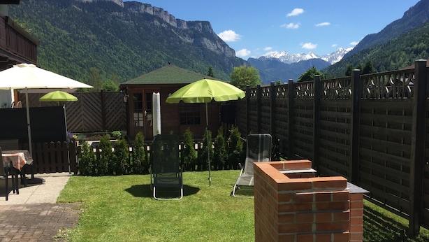 A well-maintained outdoor patio area with a brick barbecue, two green umbrellas, and a seating area with chairs. - Haus Alpenrose (Waidring)