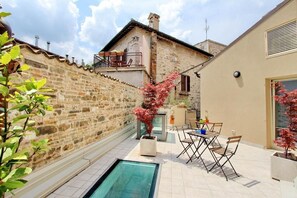 Un patio con piscina, mobiliario exterior y un muro de piedra.