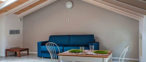 Une chambre à coucher confortable, aménagée en mezzanine, avec un plafond en pente, un canapé bleu, une table en bois sur laquelle sont posées des assiettes et une chaise blanche.