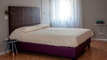 A bedroom with a bed, a small table, and a curtain.